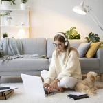 mujer trabajando desde casa (home office) sentada en el suelo junto a un perro con una laptop