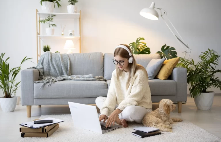 mujer trabajando desde casa (home office) sentada en el suelo junto a un perro con una laptop